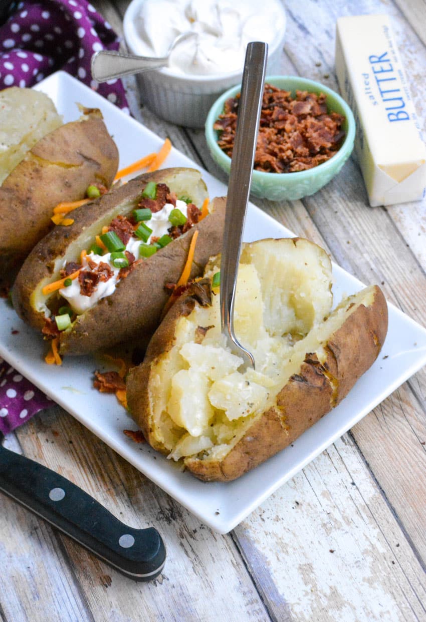 a silver fork fluffing a baked potato made in the instant pot on a white platter