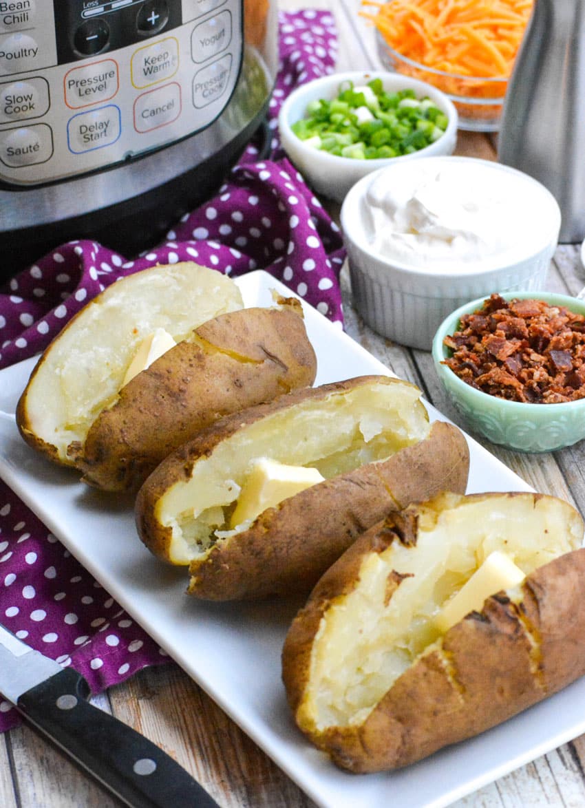 three instant pot baked potatoes arranged in a row on a white serving platter