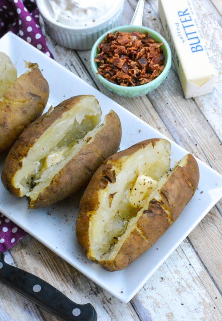 buttered and peppered instant pot baked potatoes on a white platter