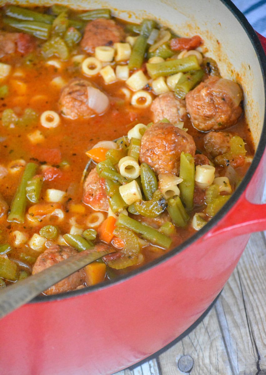 a silver ladle scooping vegetable soup with meatballs out of a large red pot