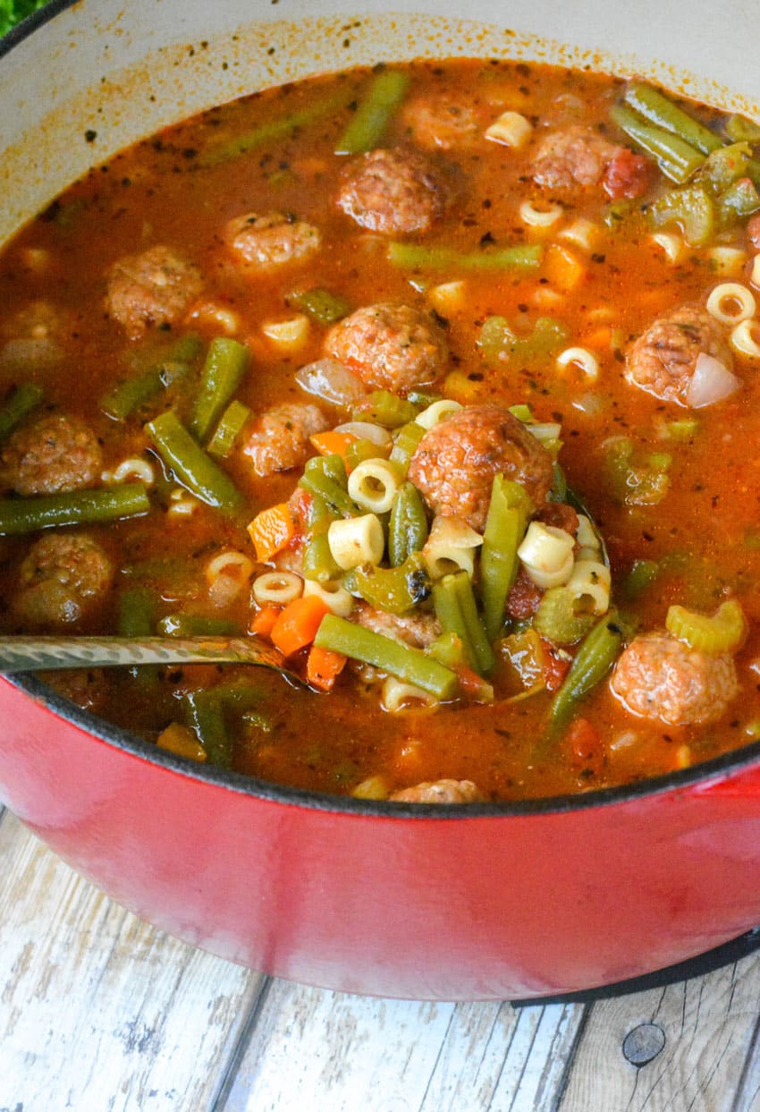 a silver ladle scooping vegetable soup with meatballs out of a large red pot