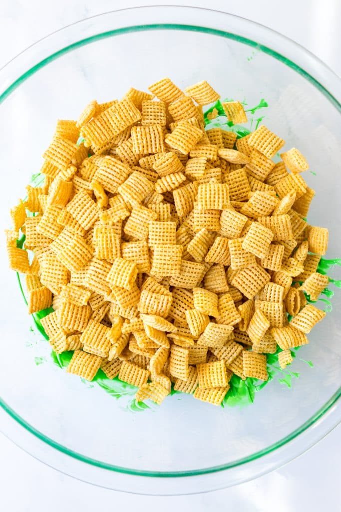 square rice cereal and melted green chocolate in a glass mixing bowl