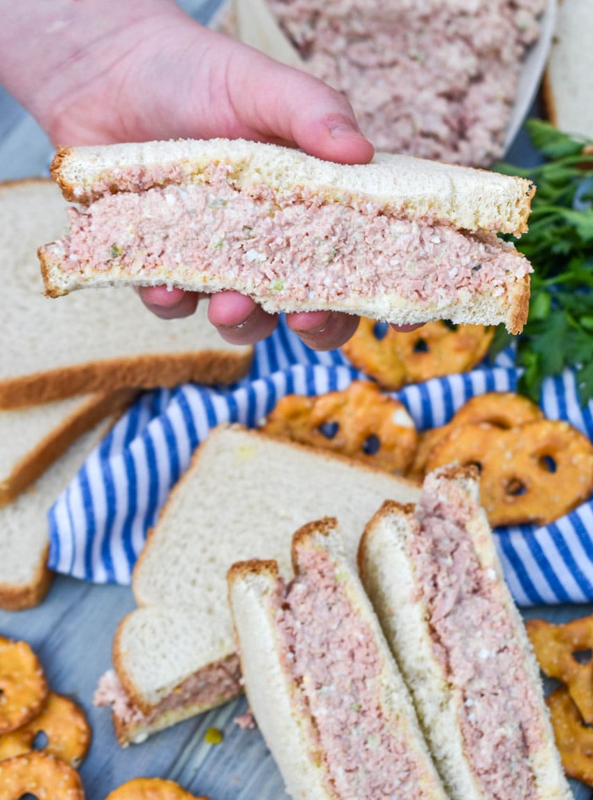 a hand holding up half a bologna salad sandwich