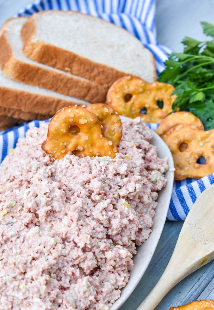 old fashioned bologna salad in a white dish with a pretzel chip stuck in the center