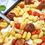 a silver spatula on a sheet pan with baked gnocchi with tomatoes and meatballs