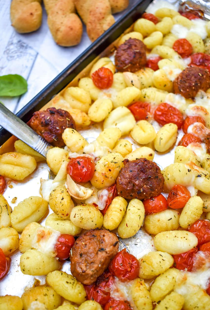 a silver spatula on a sheet pan with baked gnocchi with tomatoes and meatballs
