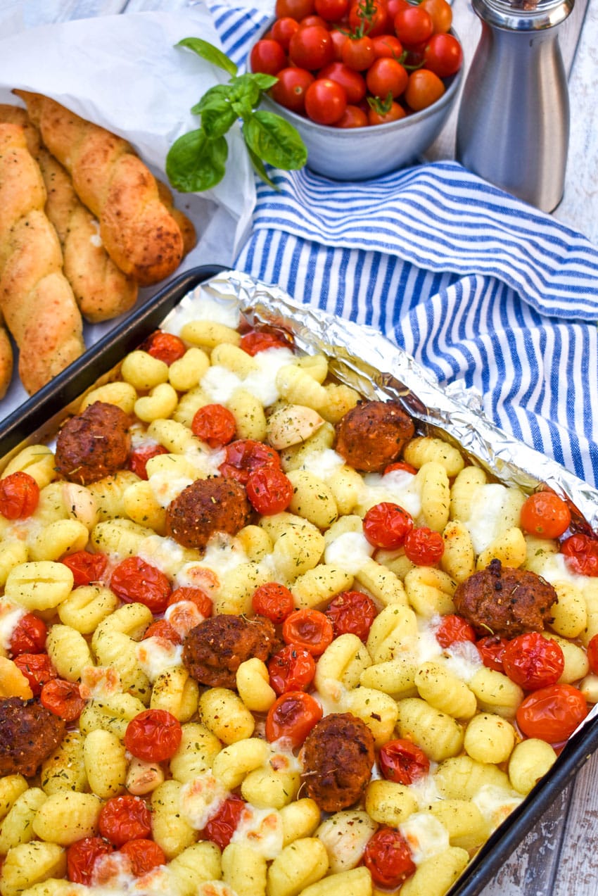 sheet pan gnocchi bake with meatballs next to baked breadsticks and a bowl of ripe cherry tomatoes