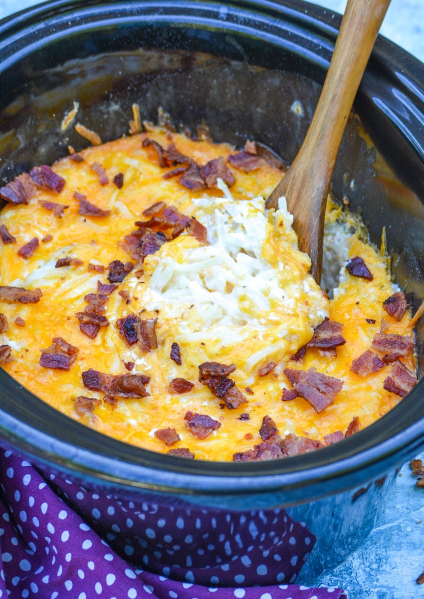 a wooden spoon stuck in a black crock filled with Slow cooker cheddar bacon ranch hash browns
