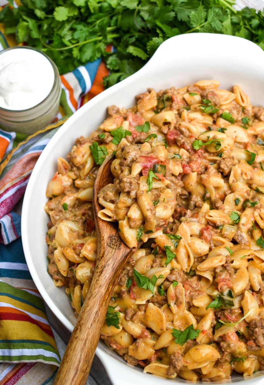 a wooden spoon in a white serving bowl filled with tex mex mac and cheese