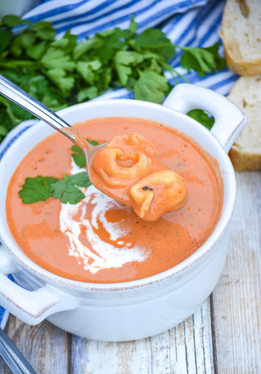 a silver spoon holding up a scoop of Three ingredient creamy tomato soup with tortellini above a white bowl