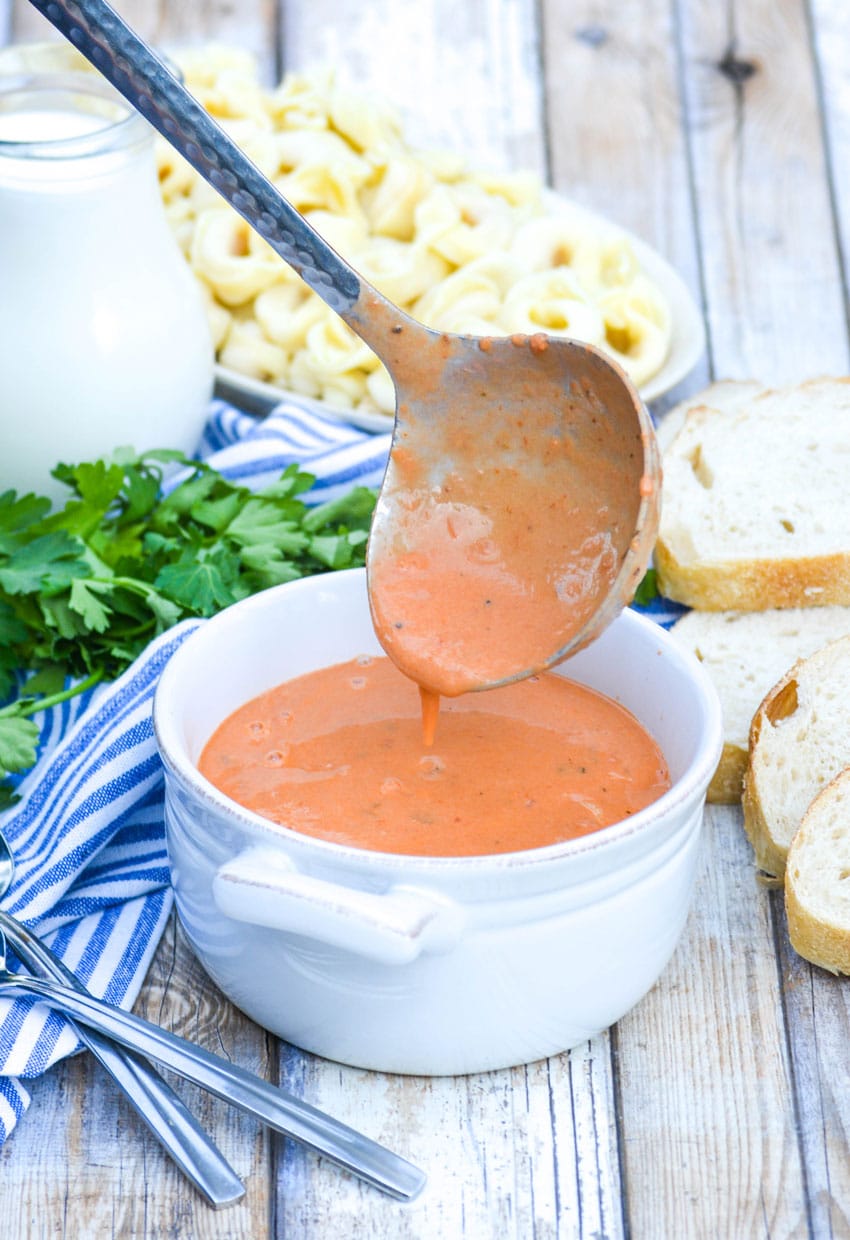 a silver ladle pouring quick and easy creamy tomato soup into a white bowl