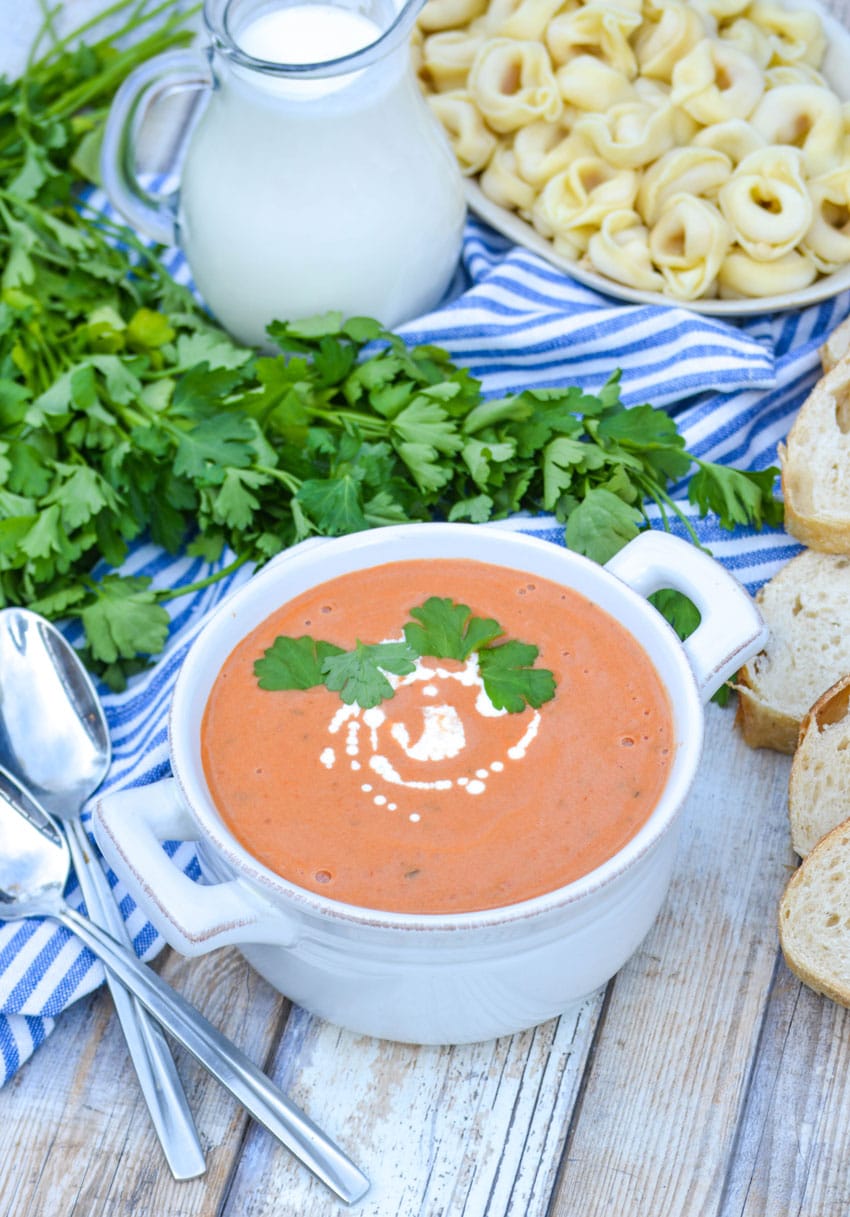 Three ingredient creamy tomato soup with tortellini in a white bowl topped with fresh cream and green herbs