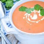 Three ingredient creamy tomato soup with tortellini in a white bowl topped with fresh cream and green herbs