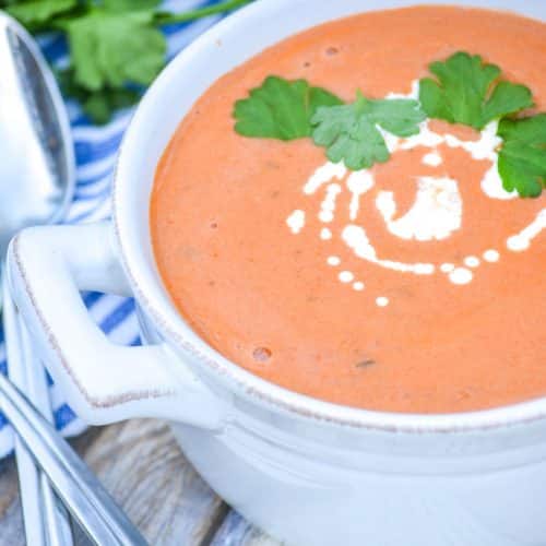 Three ingredient creamy tomato soup with tortellini in a white bowl topped with fresh cream and green herbs
