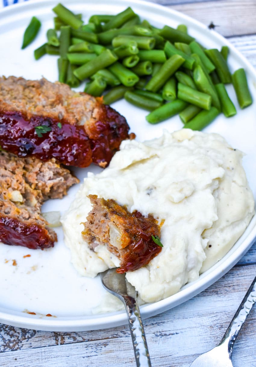 a fork dipping a piece of copycat cracker barrel meatloaf in mashed potatoes