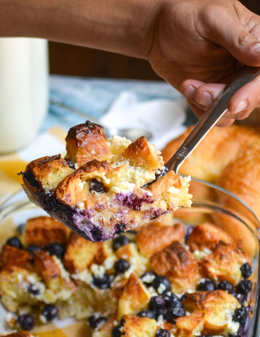 a silver spatula holding up a slice of blueberry breakfast bake with croissants