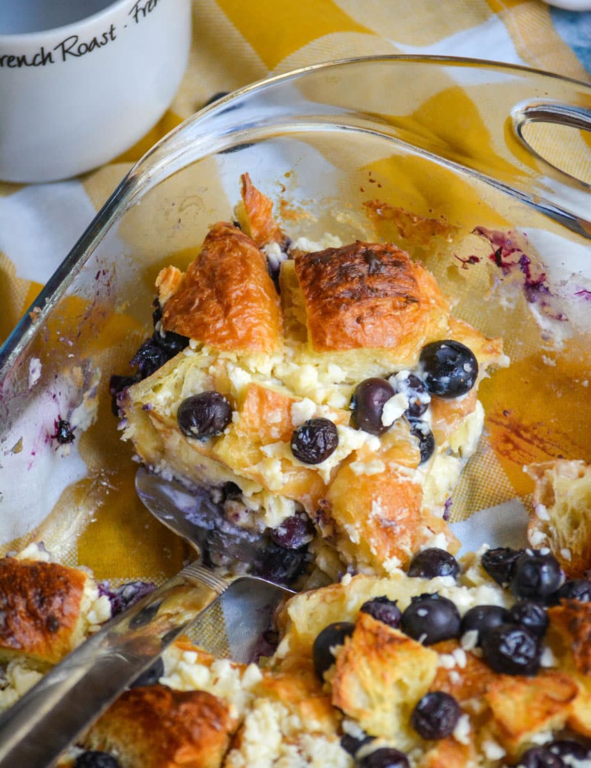 a silver spatula holding a slice of blueberry croissant bake in a glass baking dish