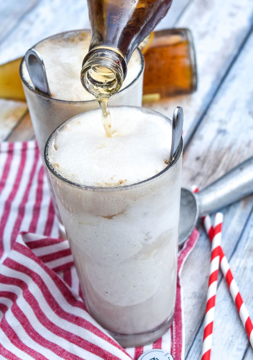 a cream soda being poured over ice cream in a tall glass