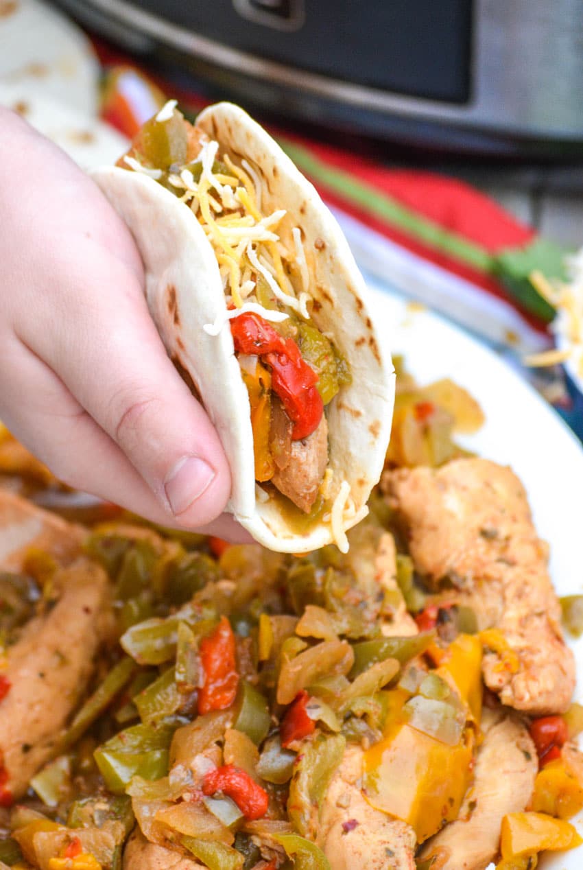 a hand holding up a flour tortilla stuffed with quick and easy chicken fajitas mixture