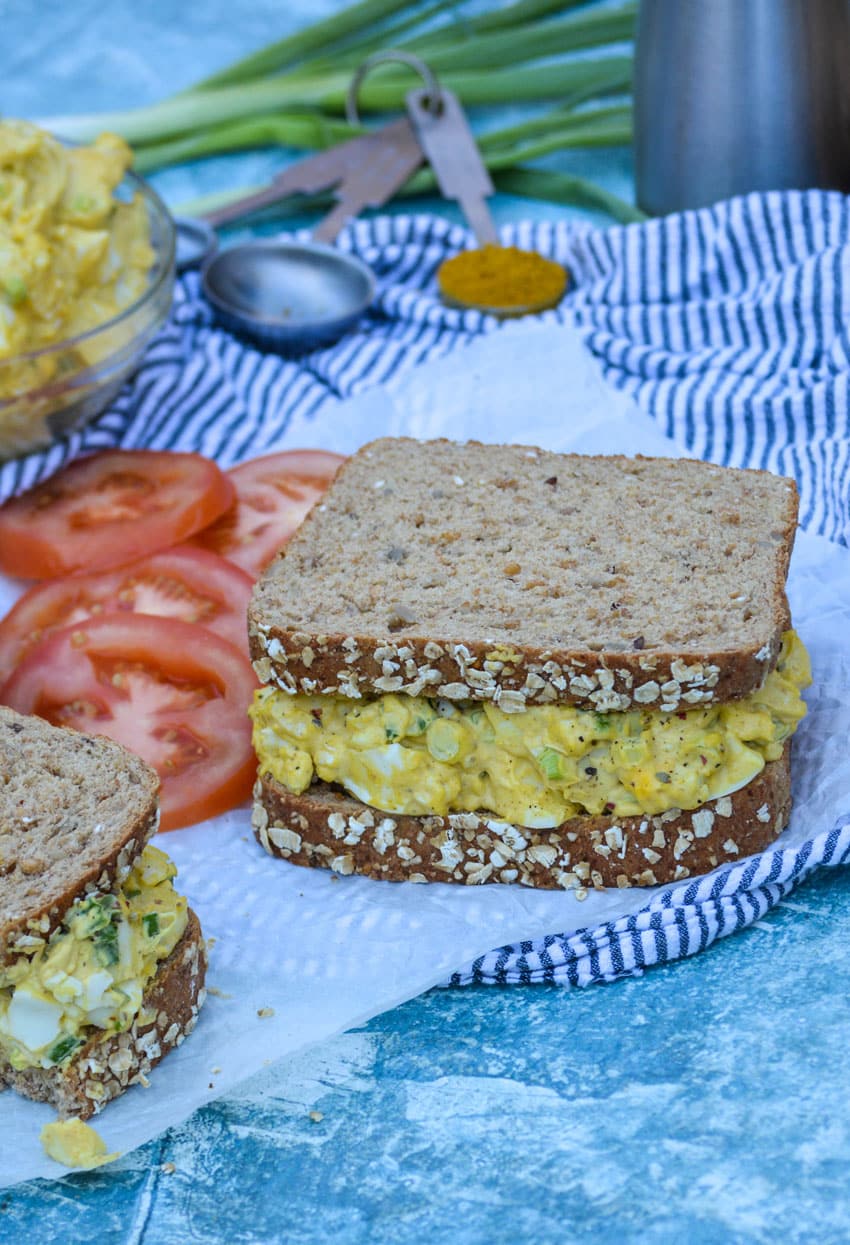 a curried egg salad sandwich resting on a sheet of white parchment paper