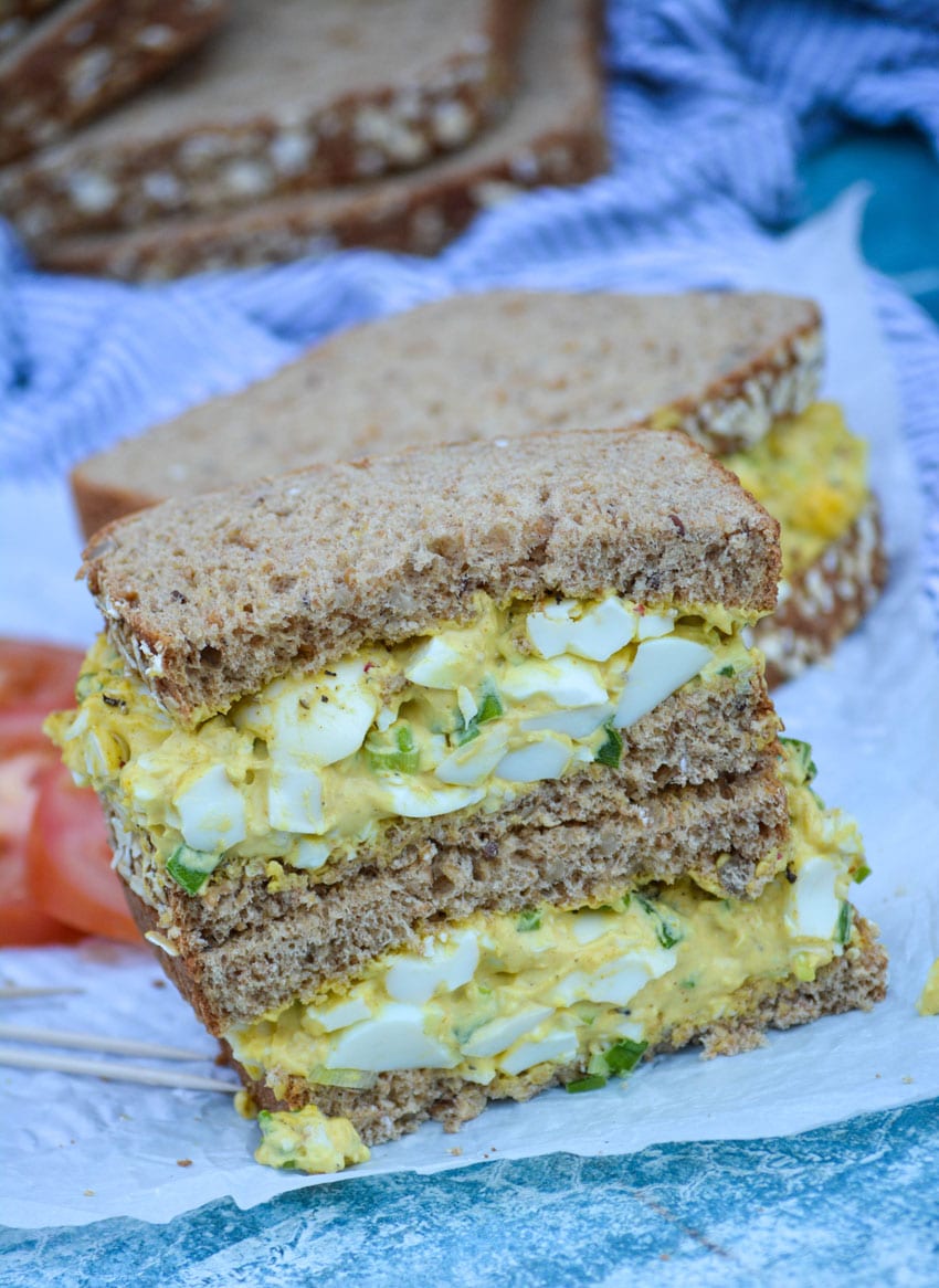 two stacked halves of curry egg salad sandwiches on white parchment paper