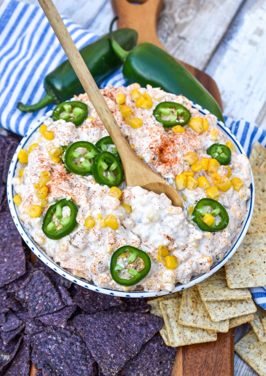 a wooden spoon in a white bowl filled with creamy corn dip