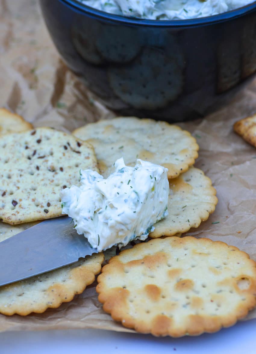 a spreader topped with whipped cream cheese spread with herbs resting on a pile of crackers