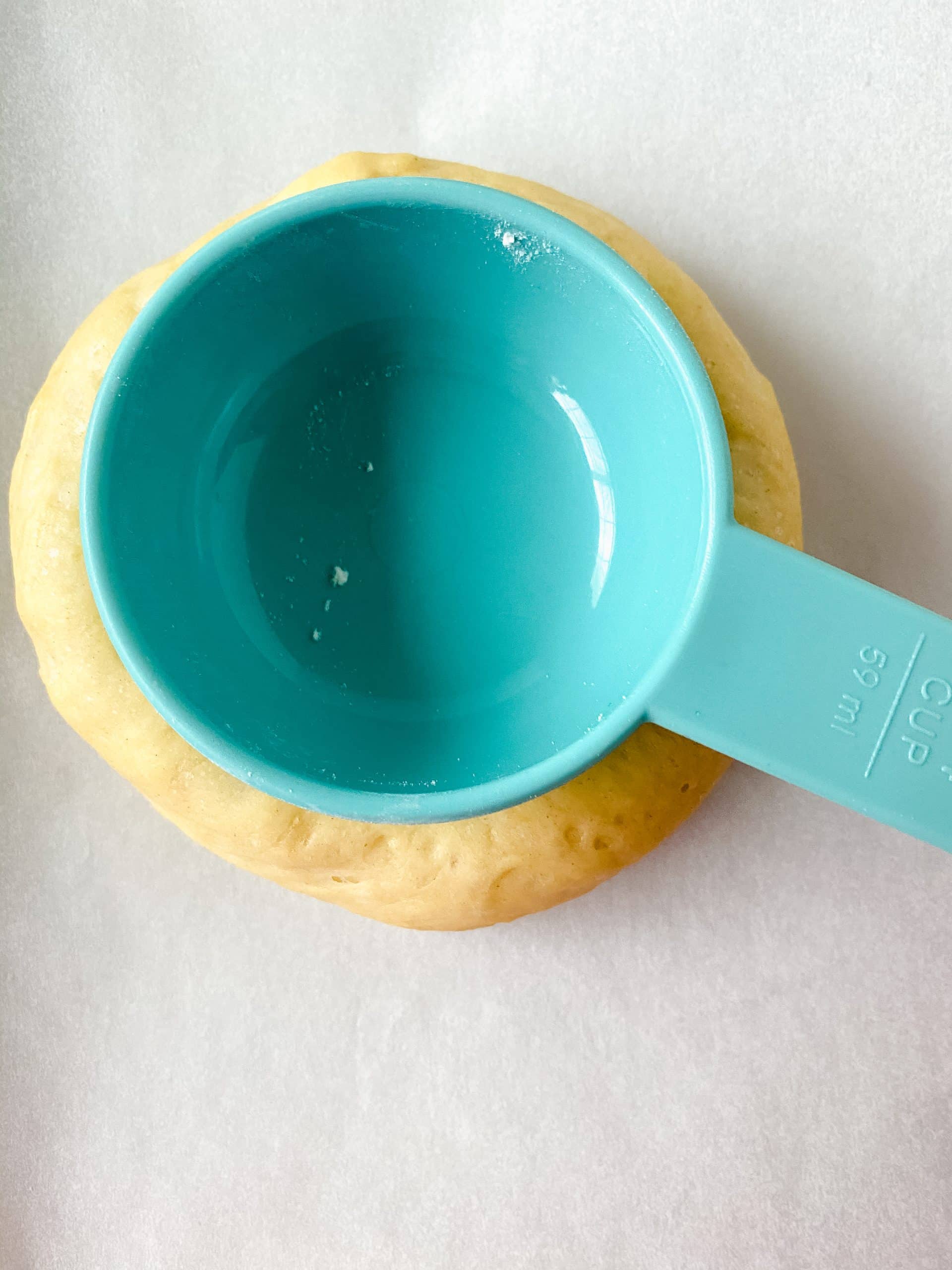 a small blue measuring cup making a well in a small ball of pastry dough