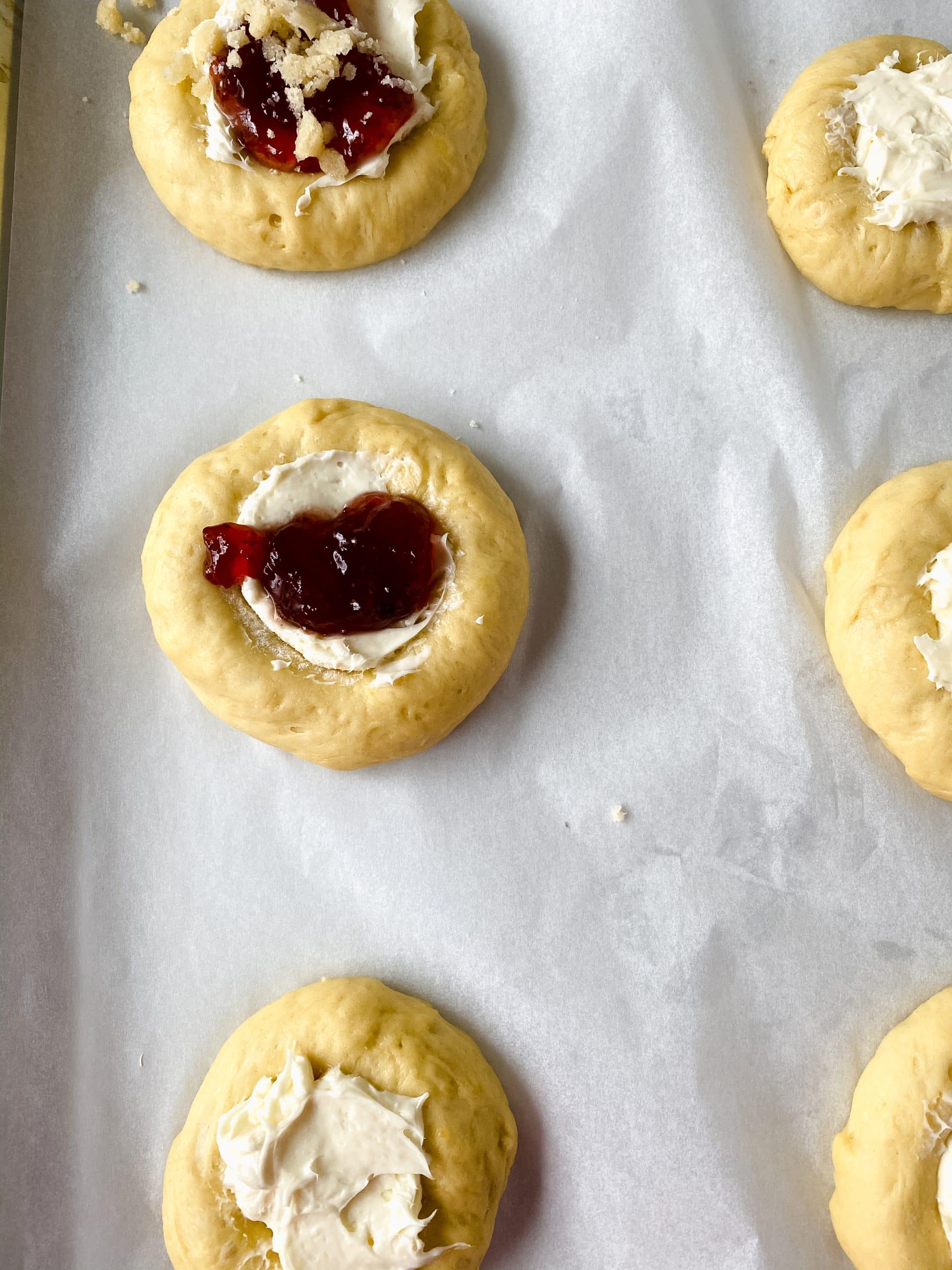 unbaked cream cheese filled danishes topped with strawberry preserves on a parchment paper lined baking sheet