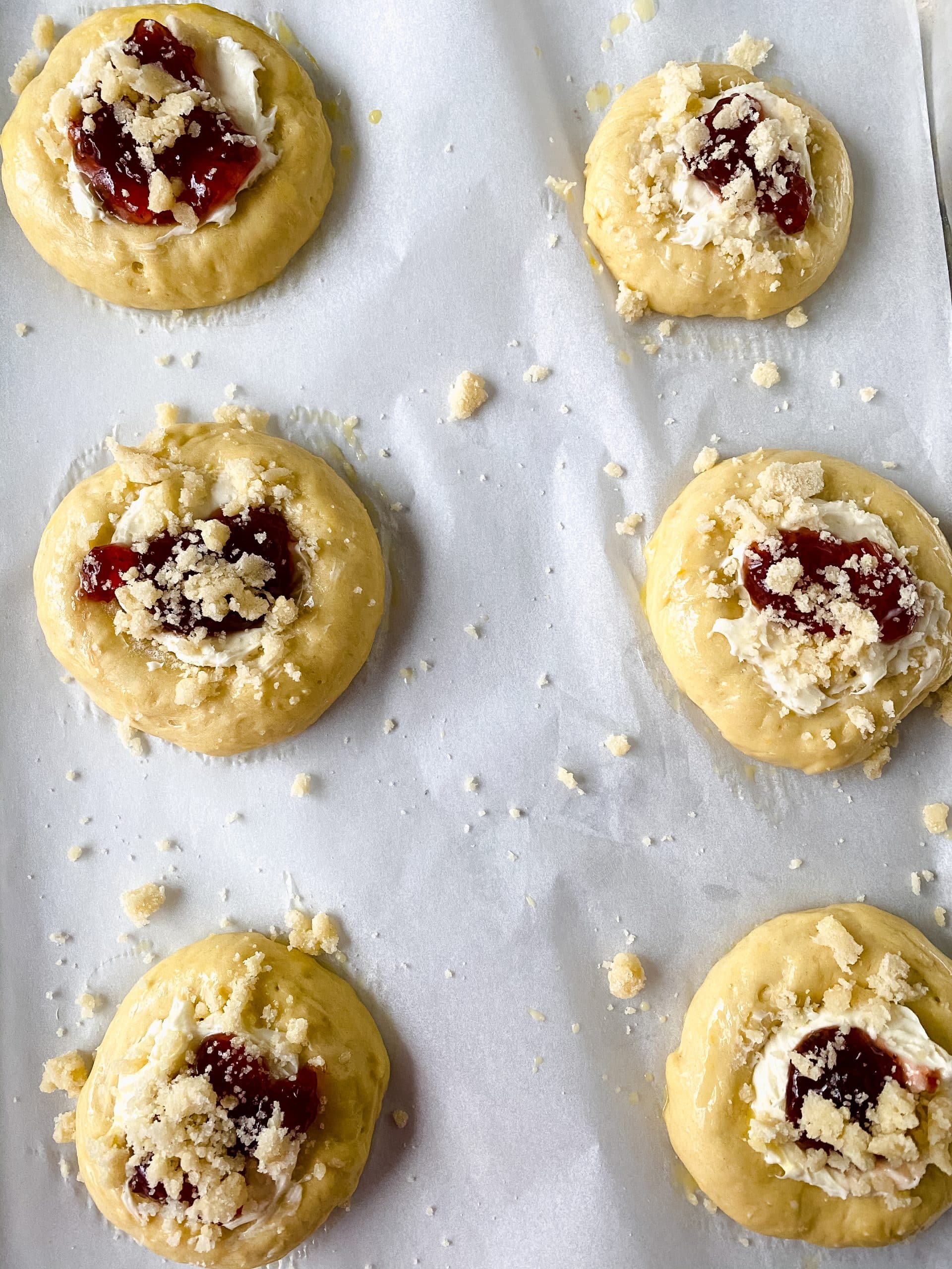 unbaked strawberry cream cheese danish on a parchment paper lined baking dish topped with a sugared crumble
