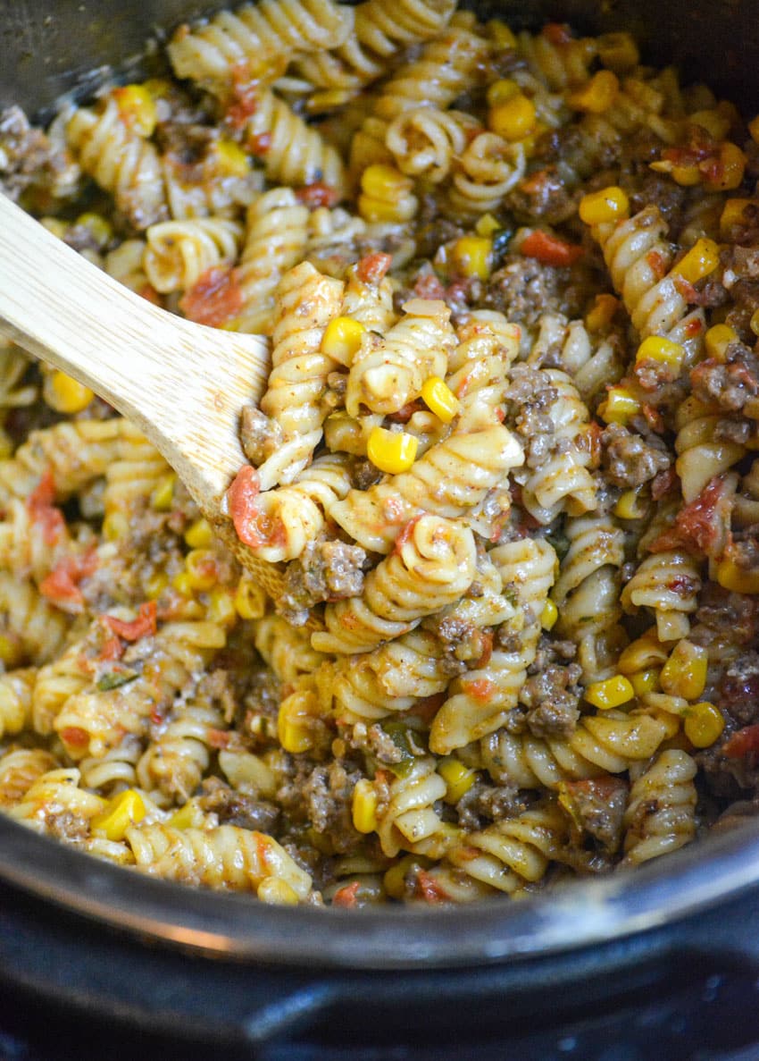a wooden spoon in a batch of cheesy taco pasta in an instant pot