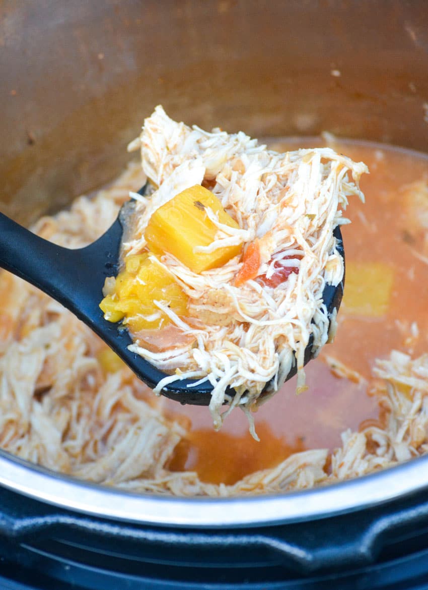 a black ladle holding up a scoop of sweet pineapple shredded chicken above an instant pot