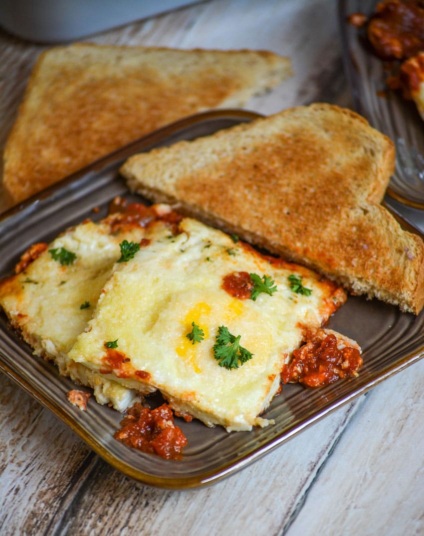 baked eggs in tomato sauce on a brown plate with toast on the side