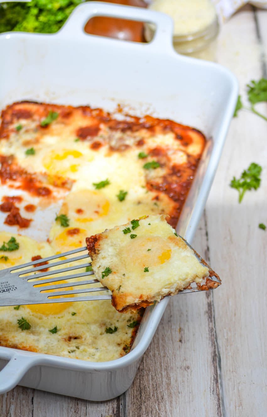 a spatula resting on the corner of a white casserole dish holding up a slice of Italian baked eggs
