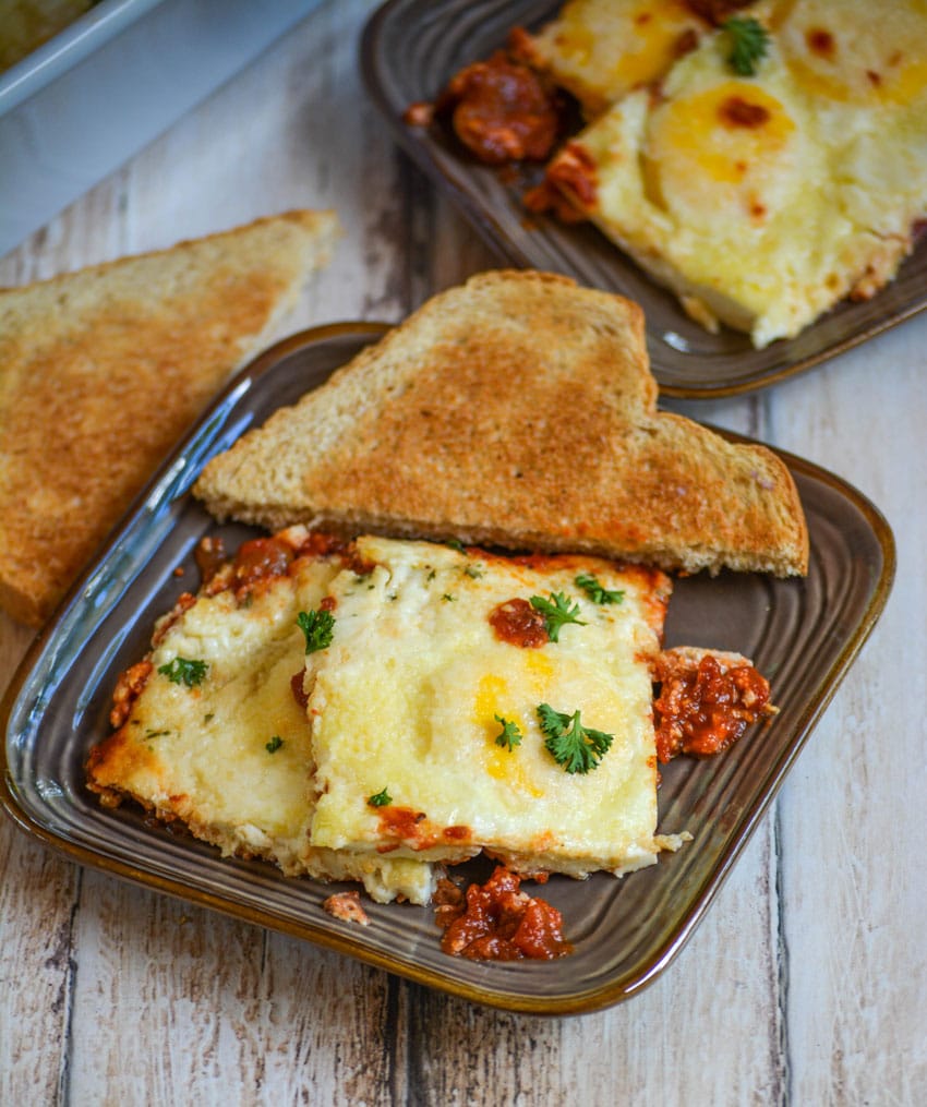 baked eggs in tomato sauce on a brown plate with toast on the side