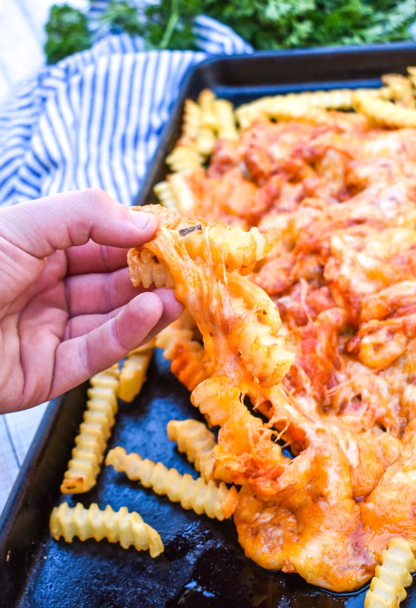 a hand holding up cheesy pizza covered fries