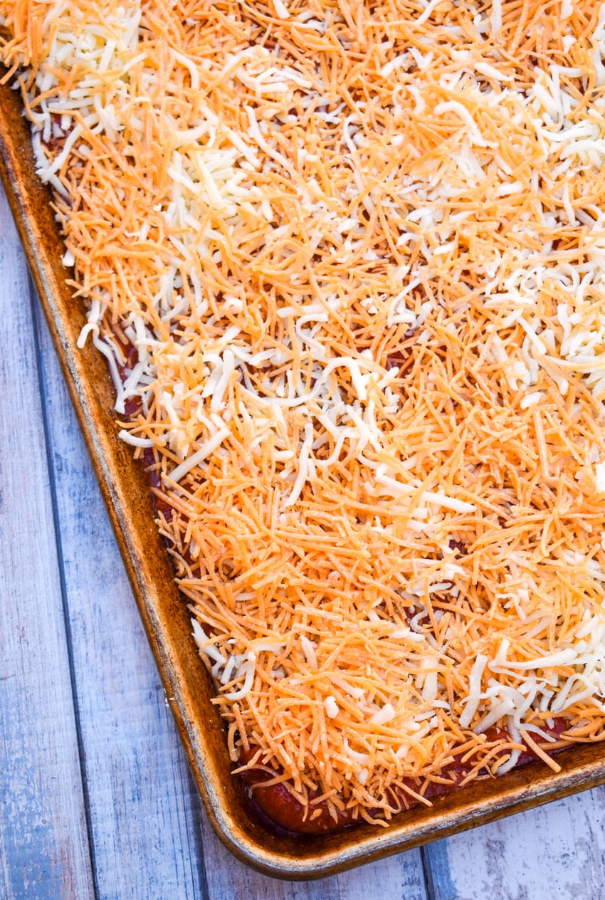 pizza sauce covered in shredded cheese on a metal baking sheet