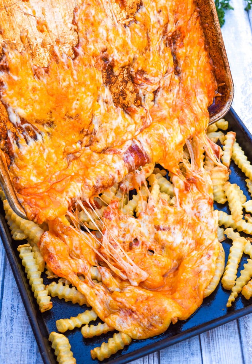 melted cheese being poured over baked french fries