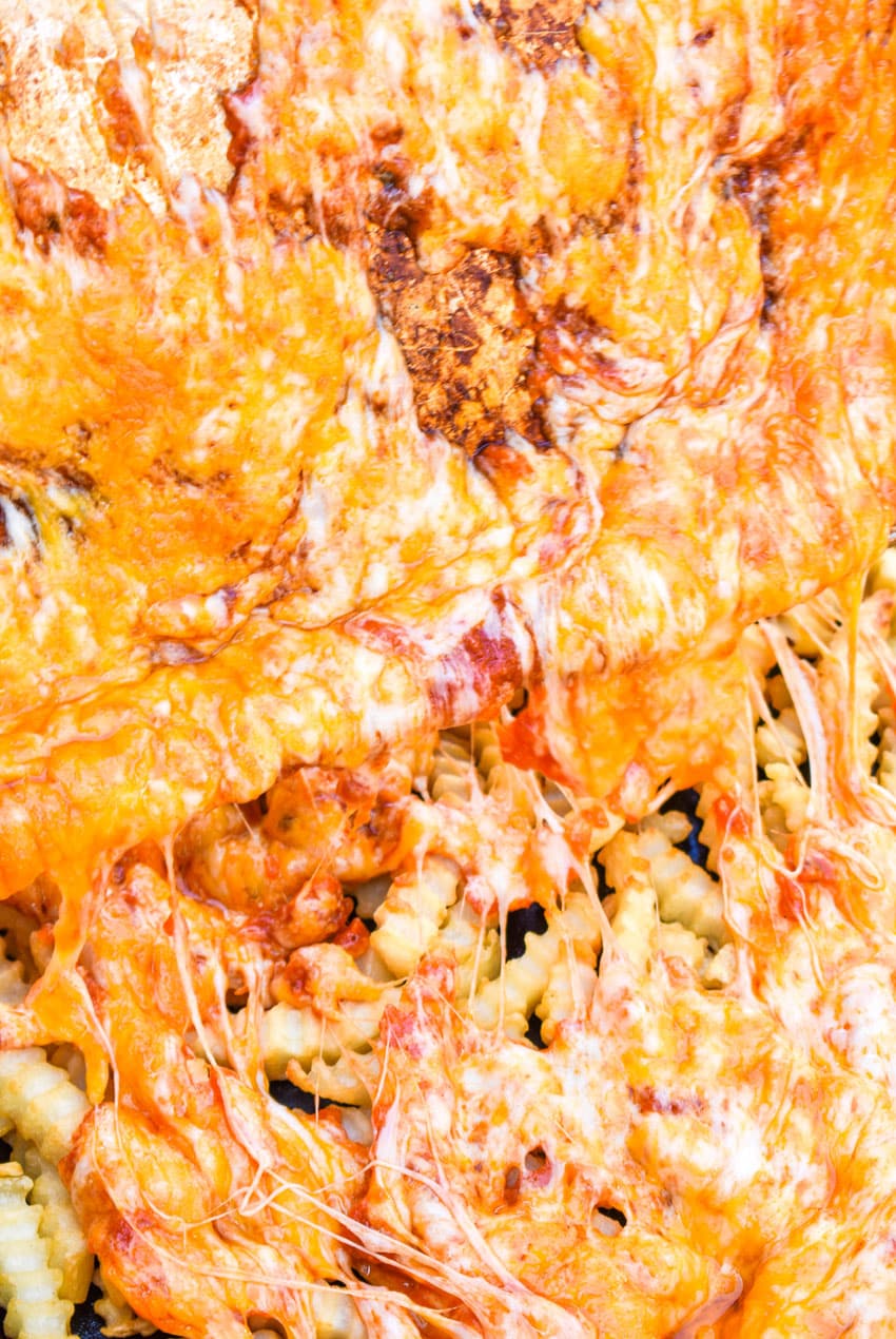melted cheese being poured over baked french fries