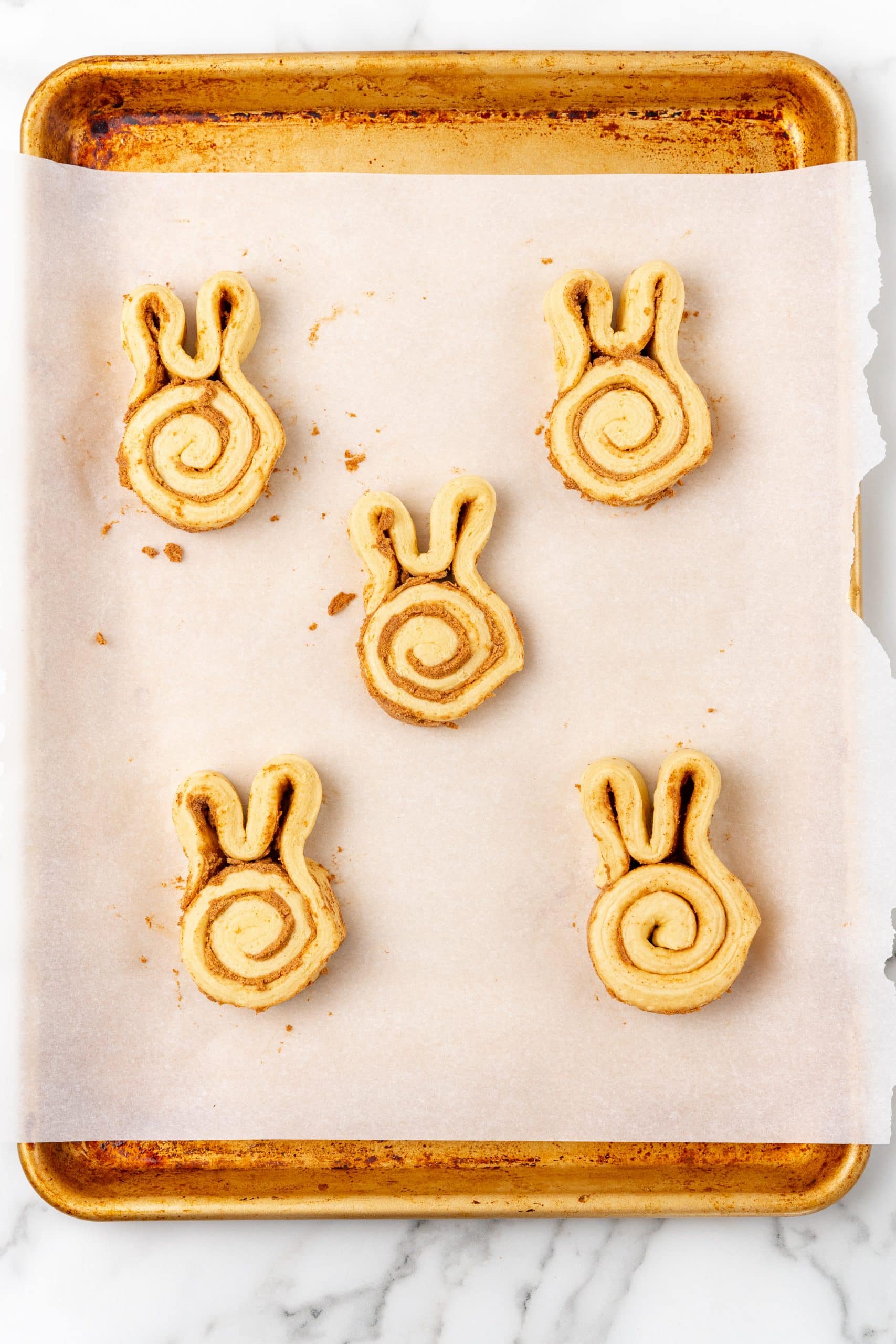 unbaked cinnamon bunny rolls on a parchment paper lined baking sheet
