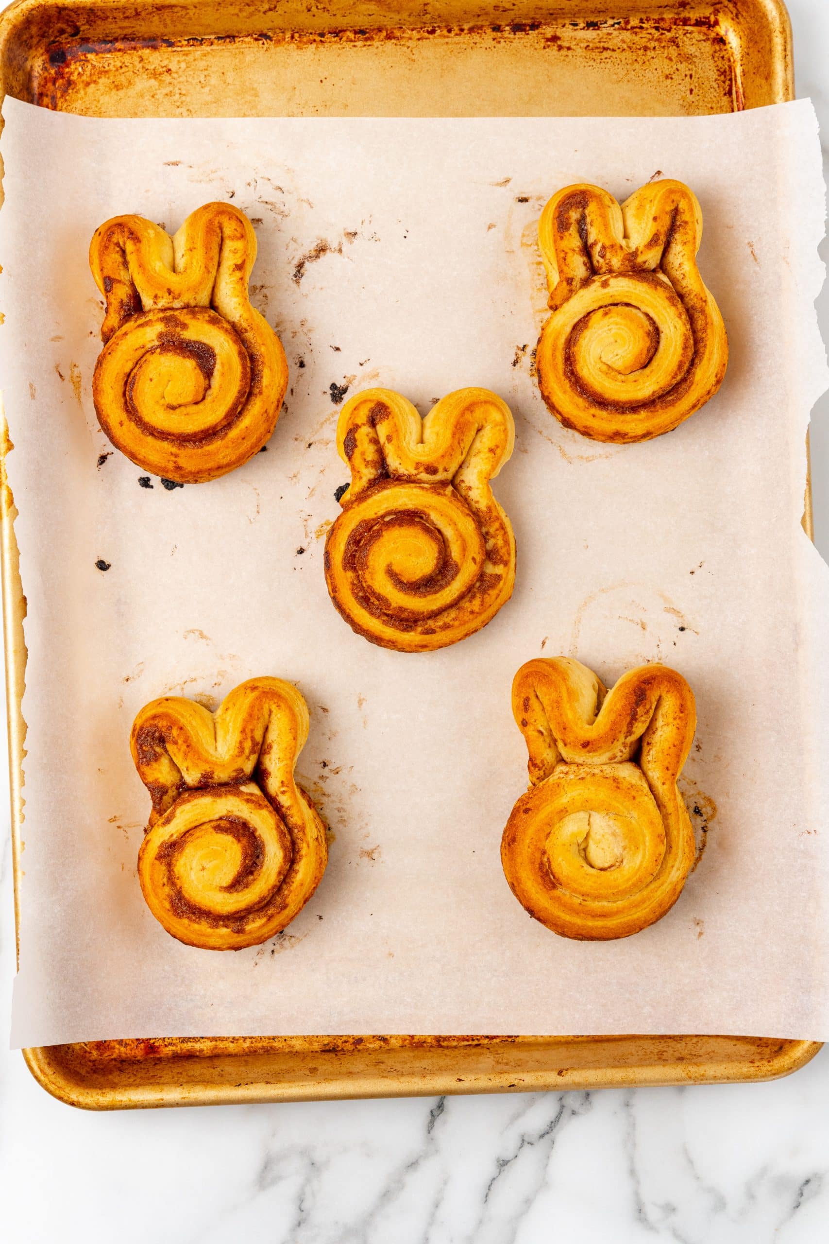baked cinnamon bunny rolls on a parchment paper lined baking sheet