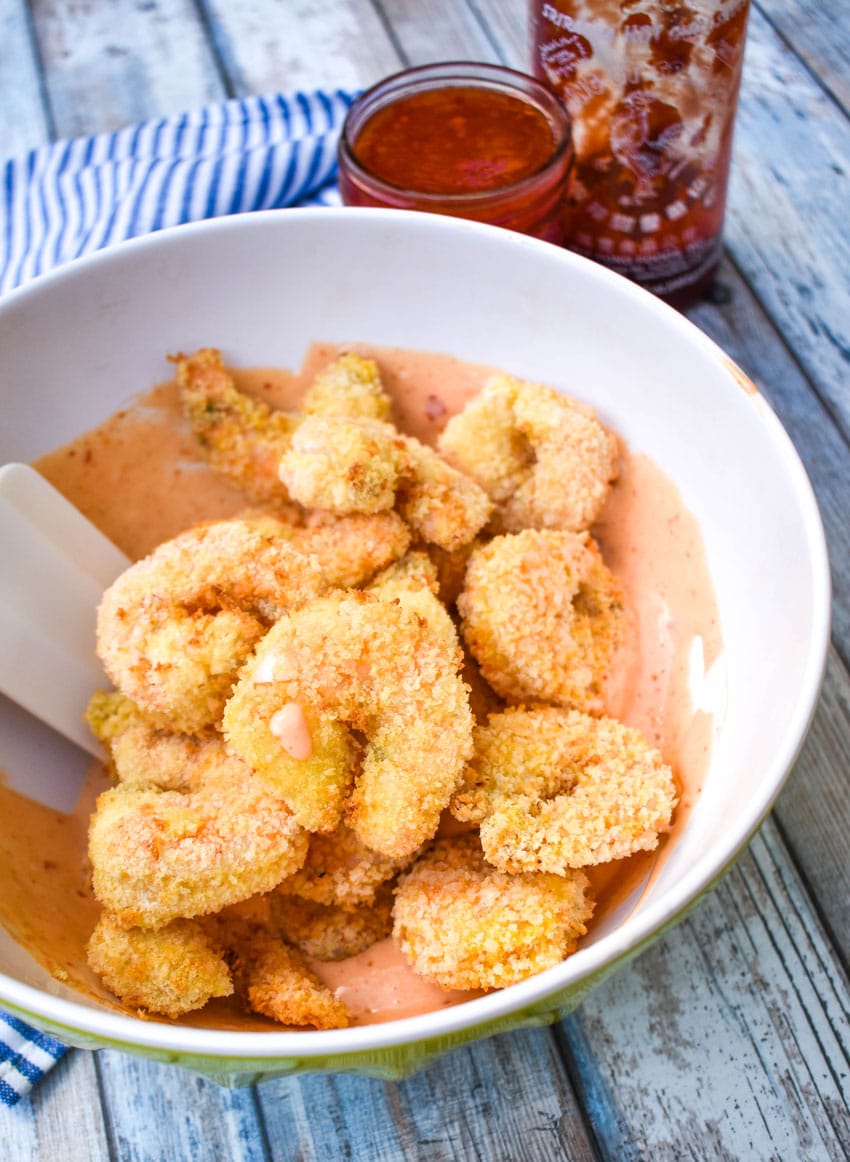 crispy air fryer shrimp in a large mixing bowl filled with bang bang sauce