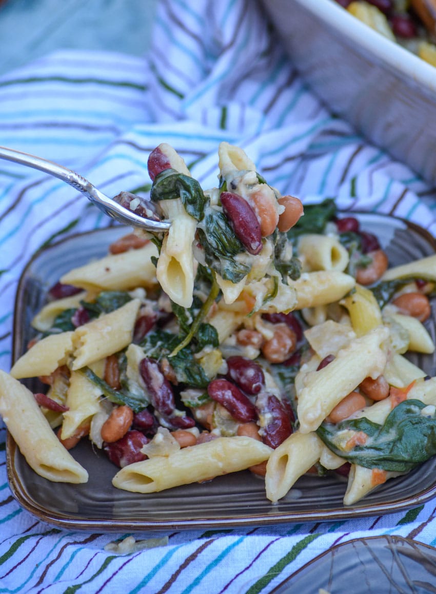 a forkful of pasta e fagioli held above a small brown plate