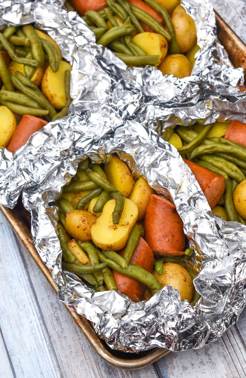 opened cajun smoked sausage foil packets on a metal baking sheets