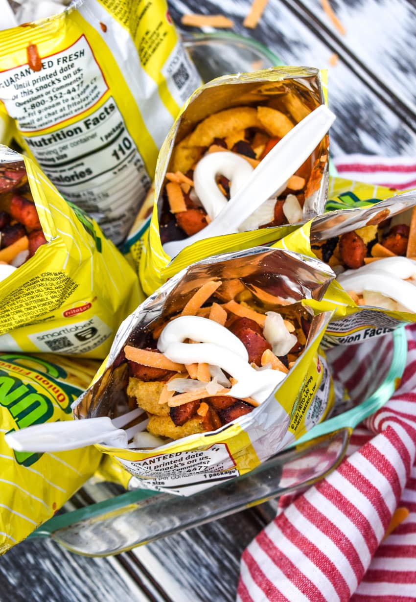 walking chili dogs arranged in a glass dish with white plastic forks stuck in them