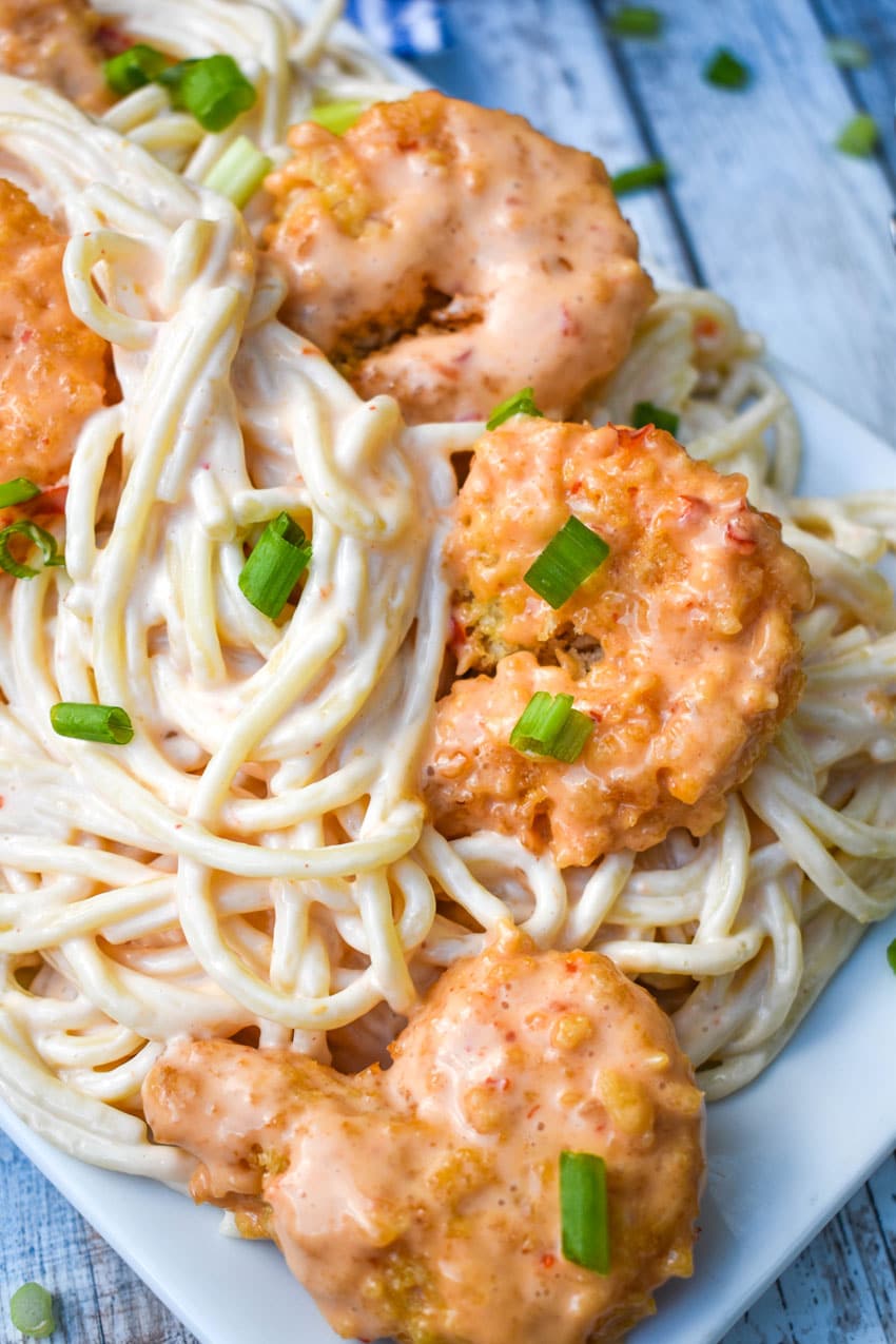 bang bang shrimp spaghetti pasta on a white platter topped with sliced green onions