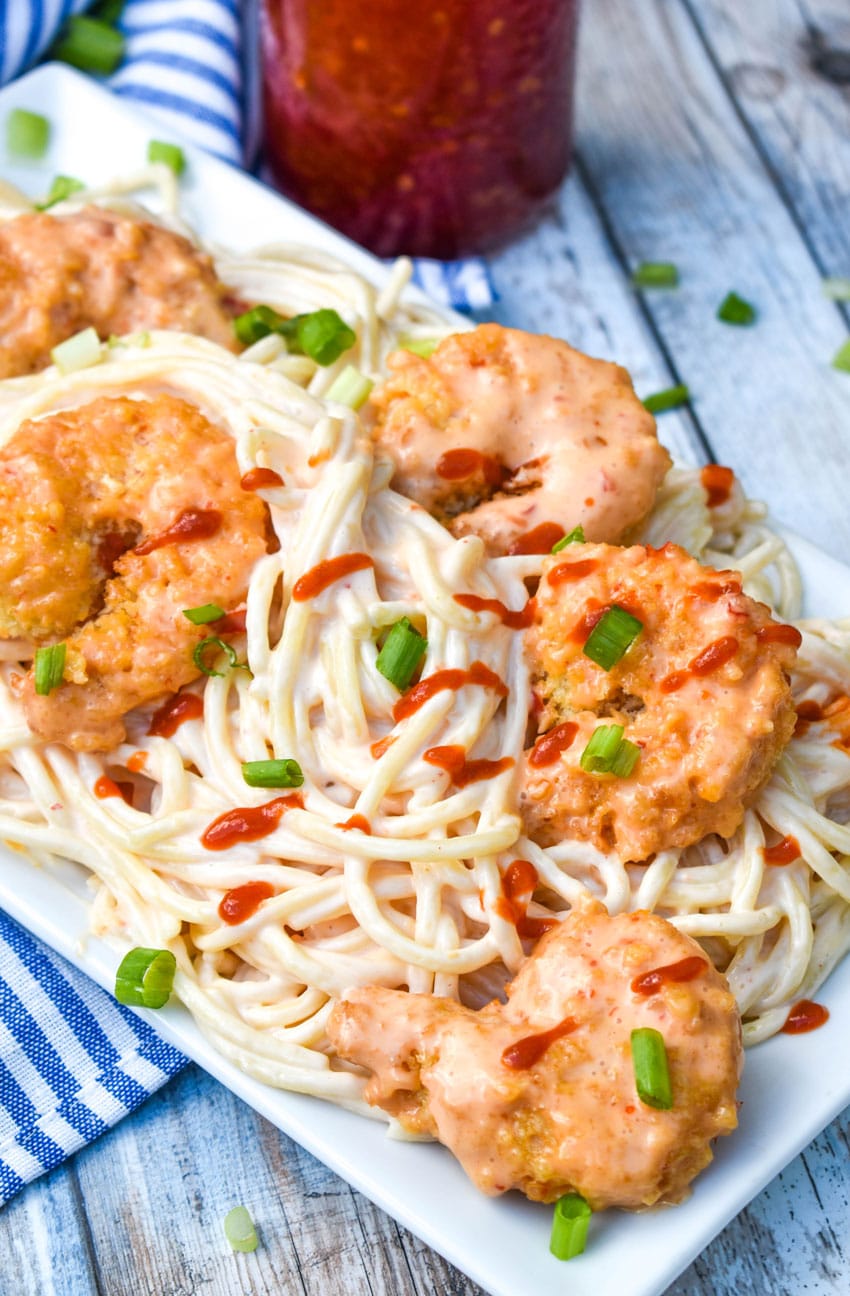 bang bang shrimp spaghetti pasta on a white platter topped with sliced green onions