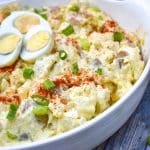 deviled egg potato salad in a white serving bowl topped with sliced green onions