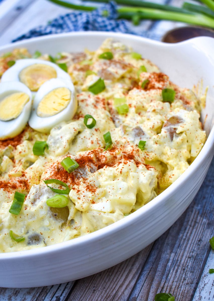 deviled egg potato salad in a white serving bowl topped with sliced green onions