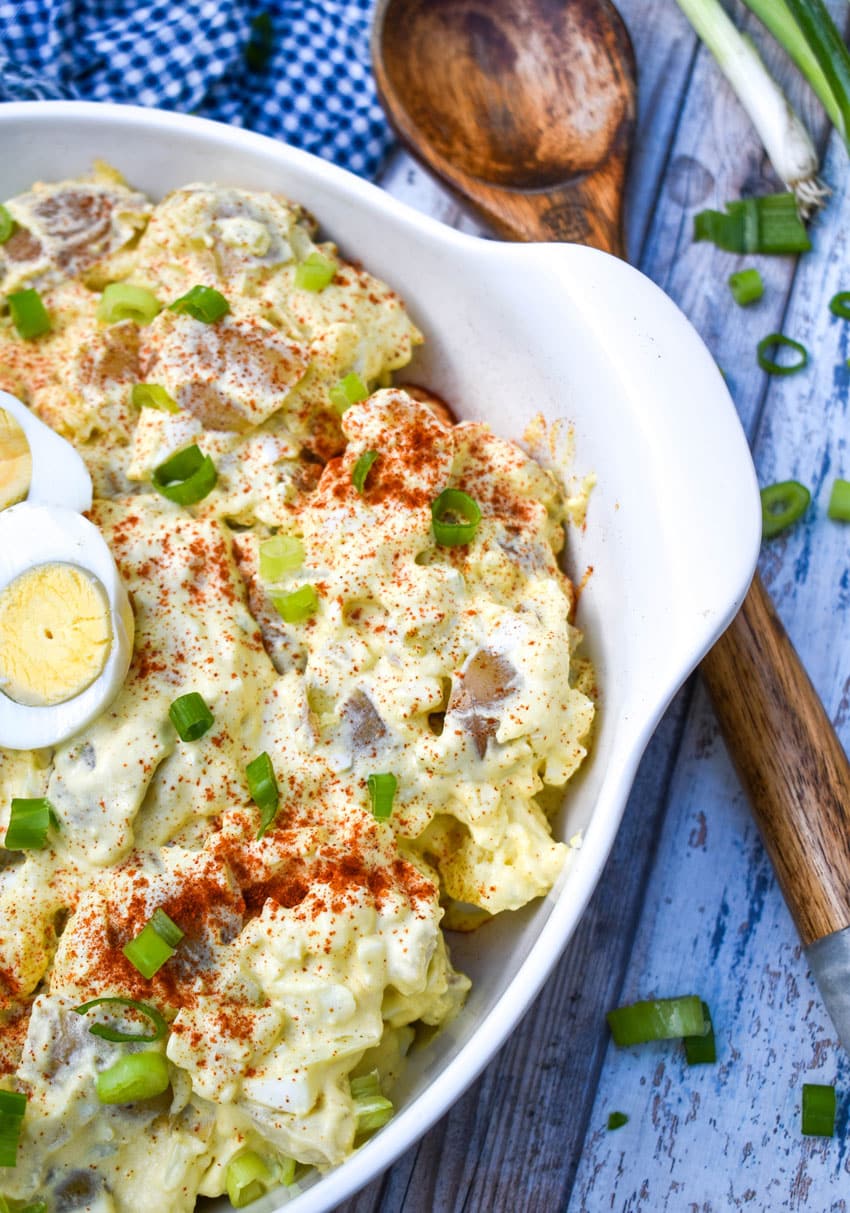 deviled egg potato salad in a white serving bowl with a wooden spoon on the side